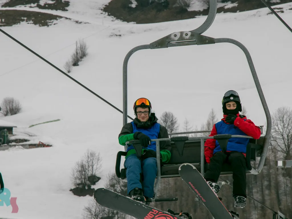 Zwei Jugendliche im Sessellift über der Piste.